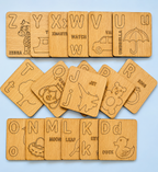 A set of wooden alphabet cards arranged in three rows on a light blue background. Each card shows a different uppercase letter from A to Z, engraved with a corresponding animal or object illustration and word.

